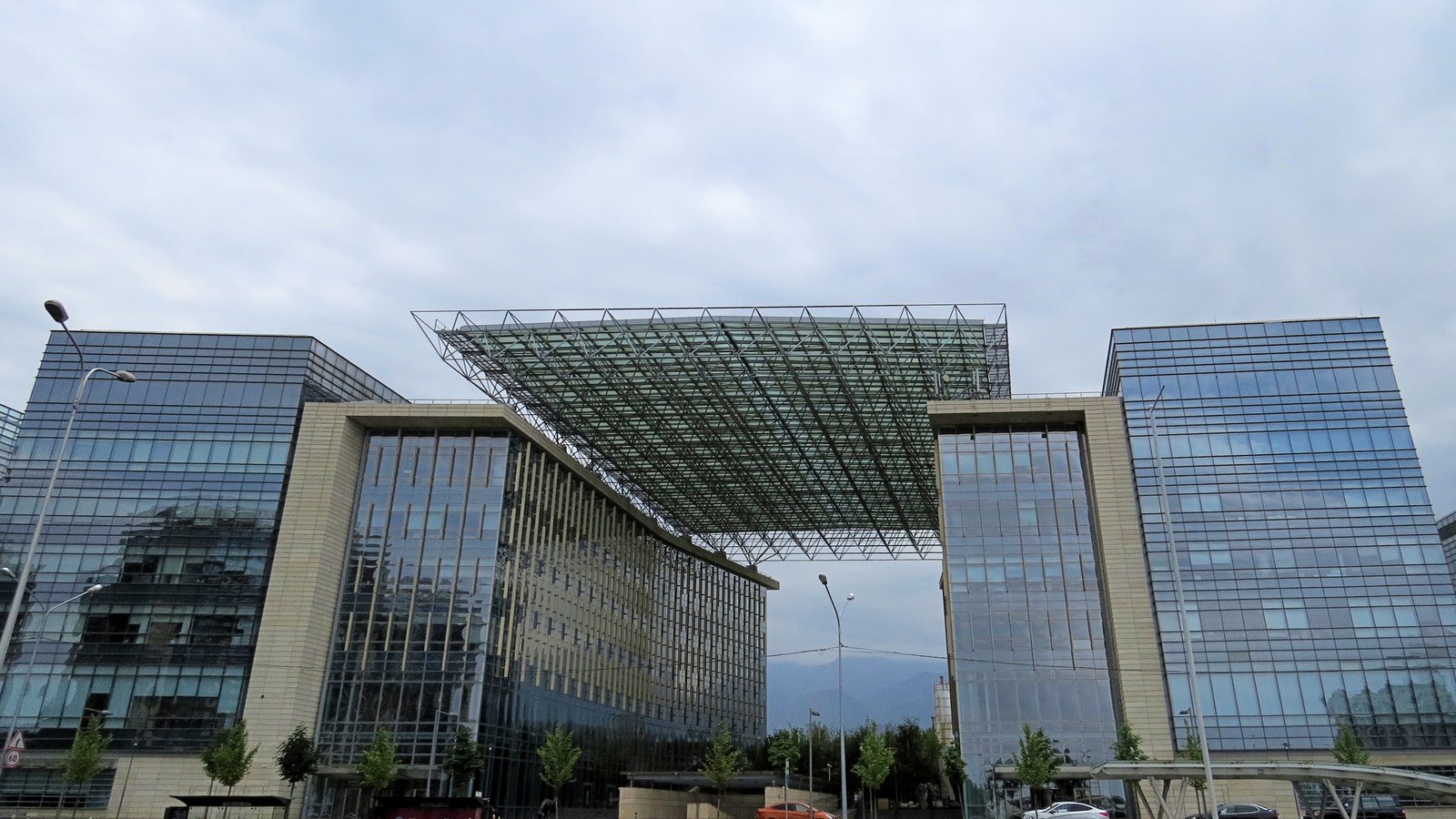 Glass office towers joined by a large steel and glass canopy under an overcast sky
