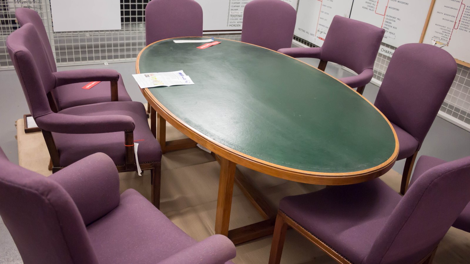 An oval green-topped boardroom table surrounded by purple upholstered chairs