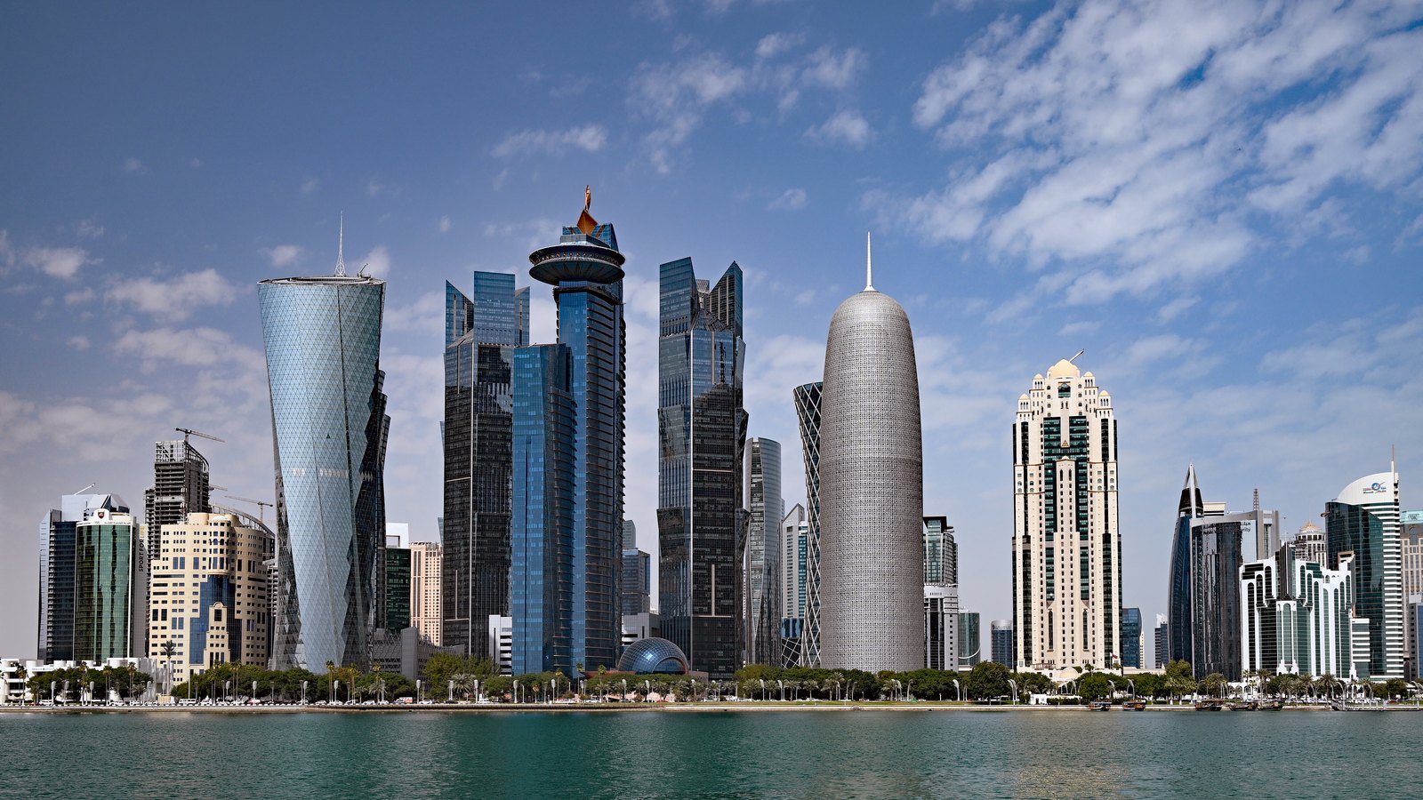 Glass skyscrapers of different shapes along the West Bay waterfront under a blue sky