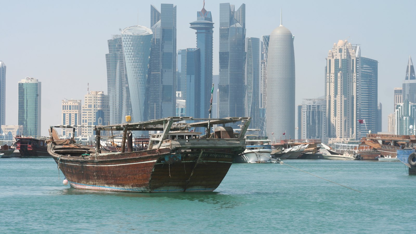 A traditional dhow on calm water in front of the high-rise towers of West Bay