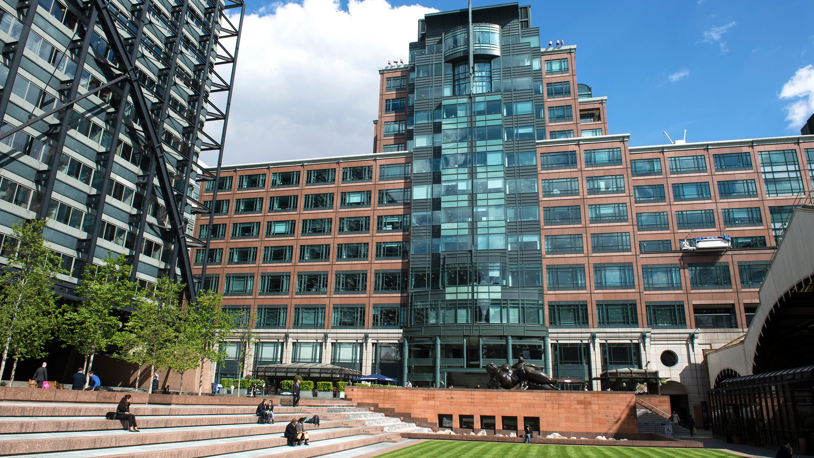 A glass and red-brick office complex rising behind a sunken lawn and steps