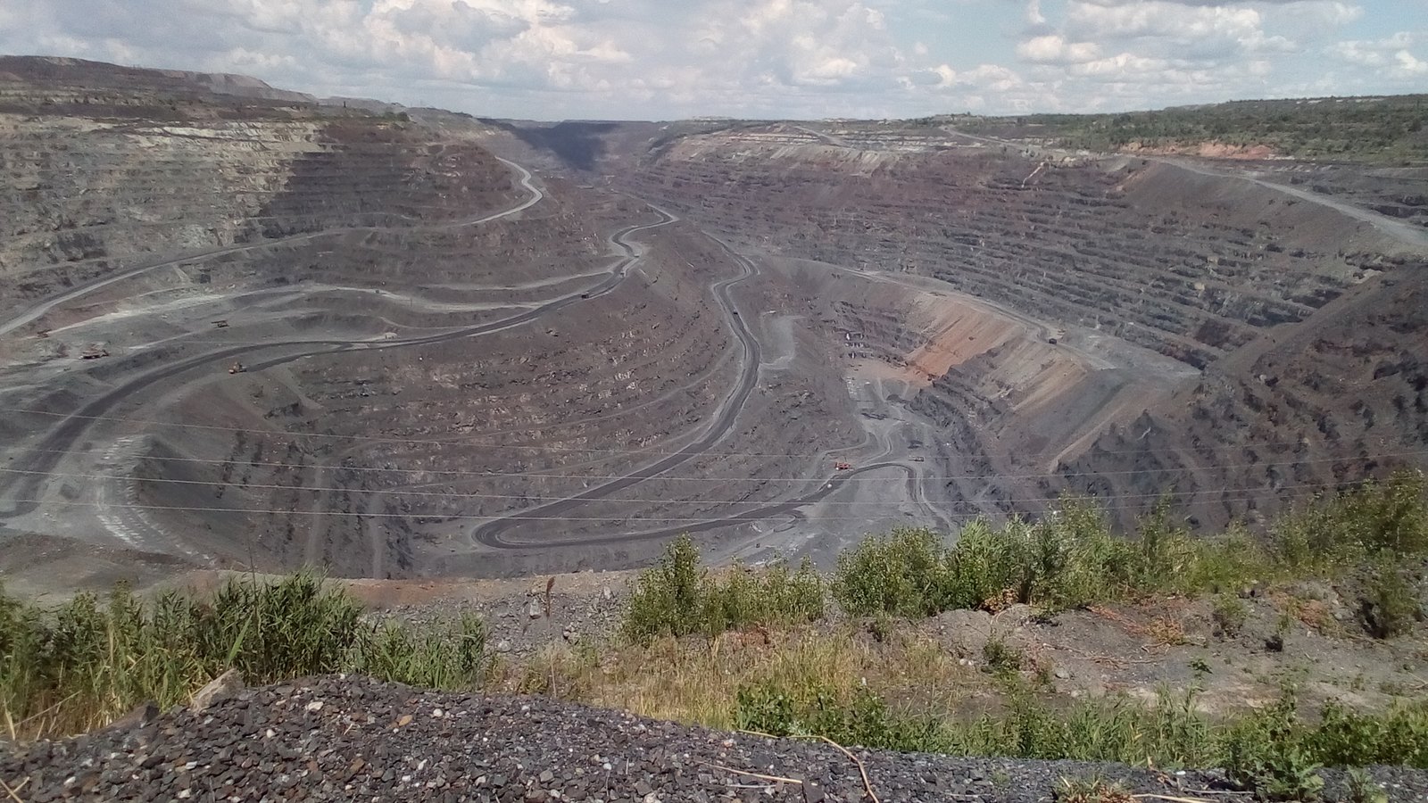 A deep open-pit quarry with terraced walls and winding haul roads, seen from its rim
