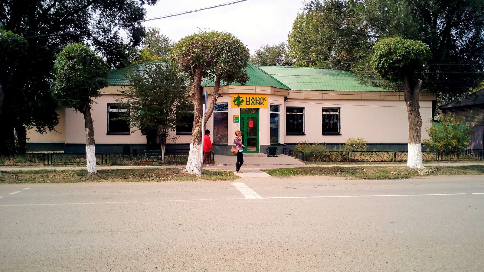 A low building with a green roof and a Halyk Bank sign over the entrance