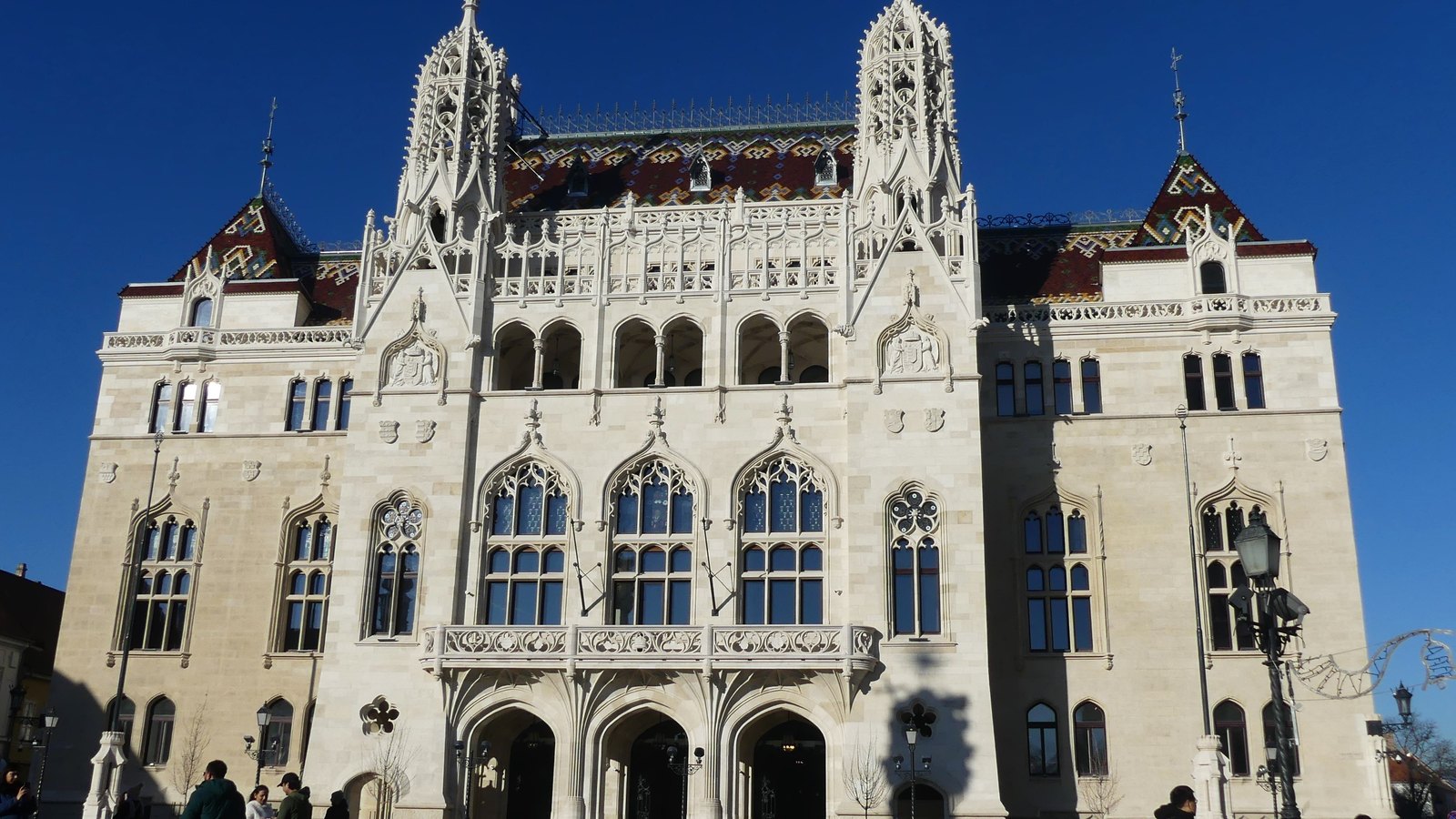A white neo-Gothic building with pointed towers and a patterned tiled roof against a deep blue sky