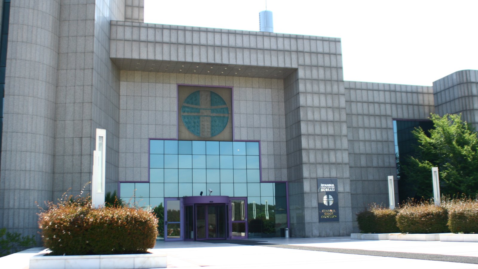 A large grey stone exchange building with a round emblem above its glass entrance