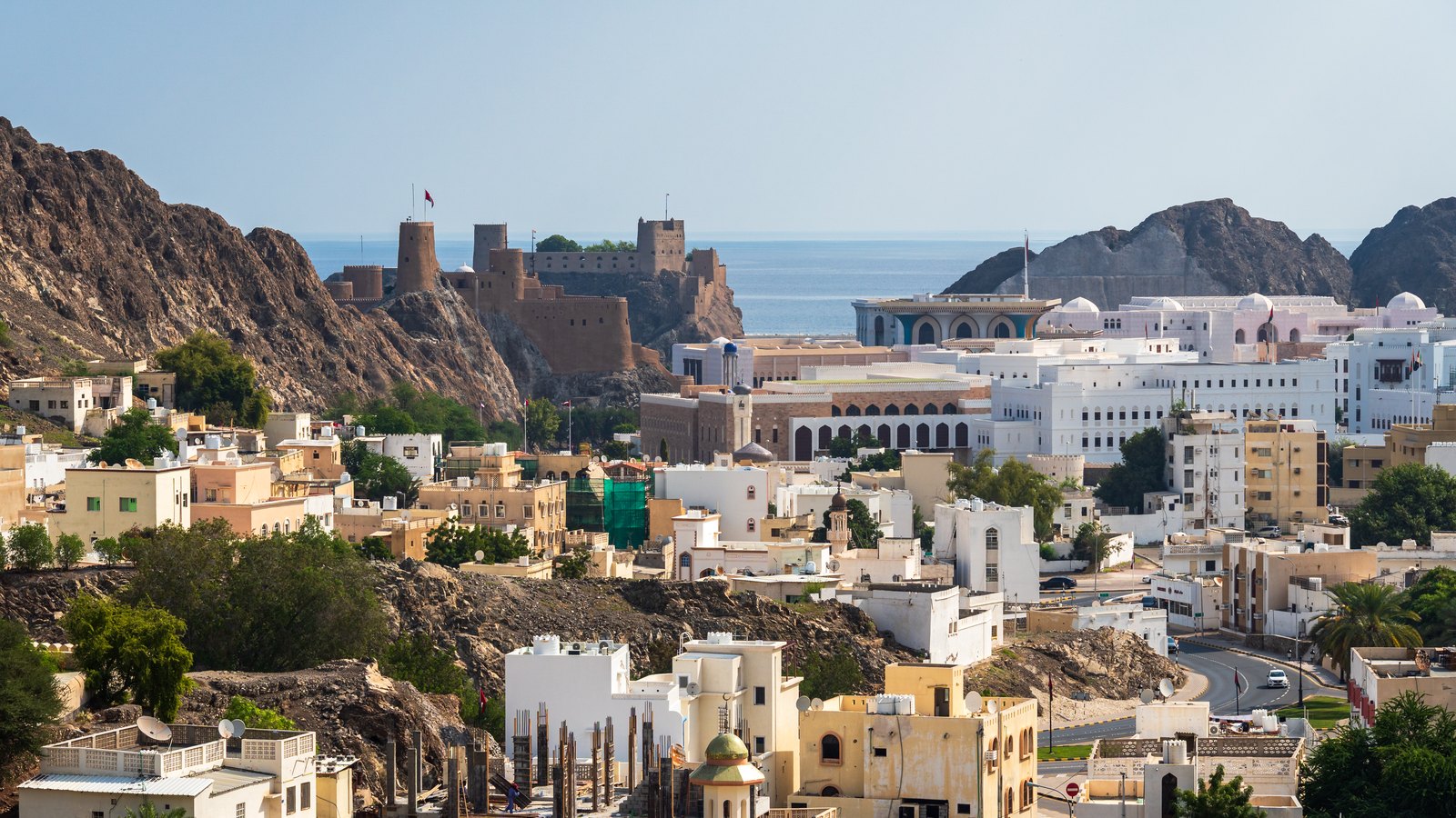 White low-rise buildings of old Muscat between rocky brown hills