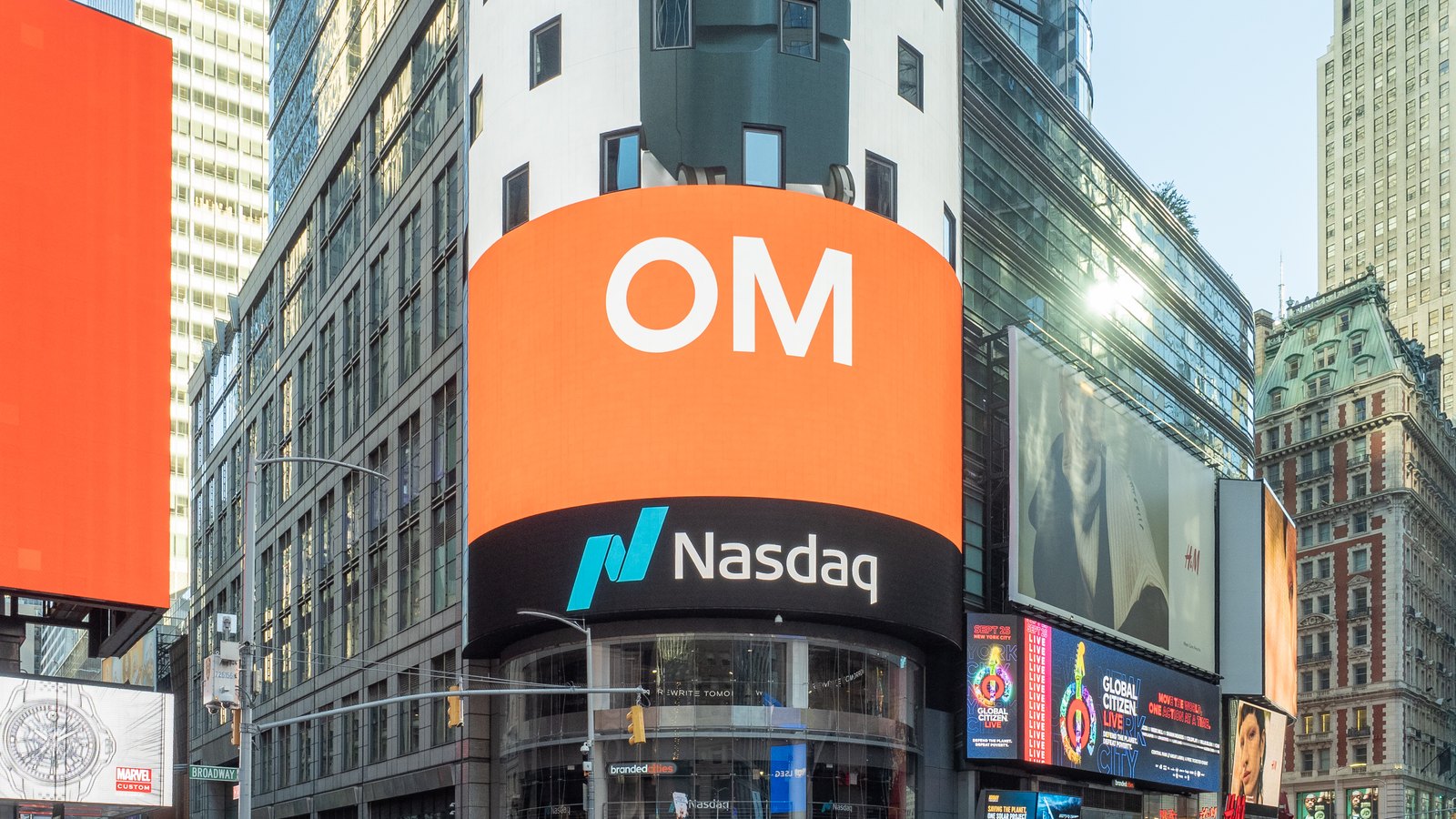 A curved tower of digital screens with the Nasdaq name above a busy Times Square street