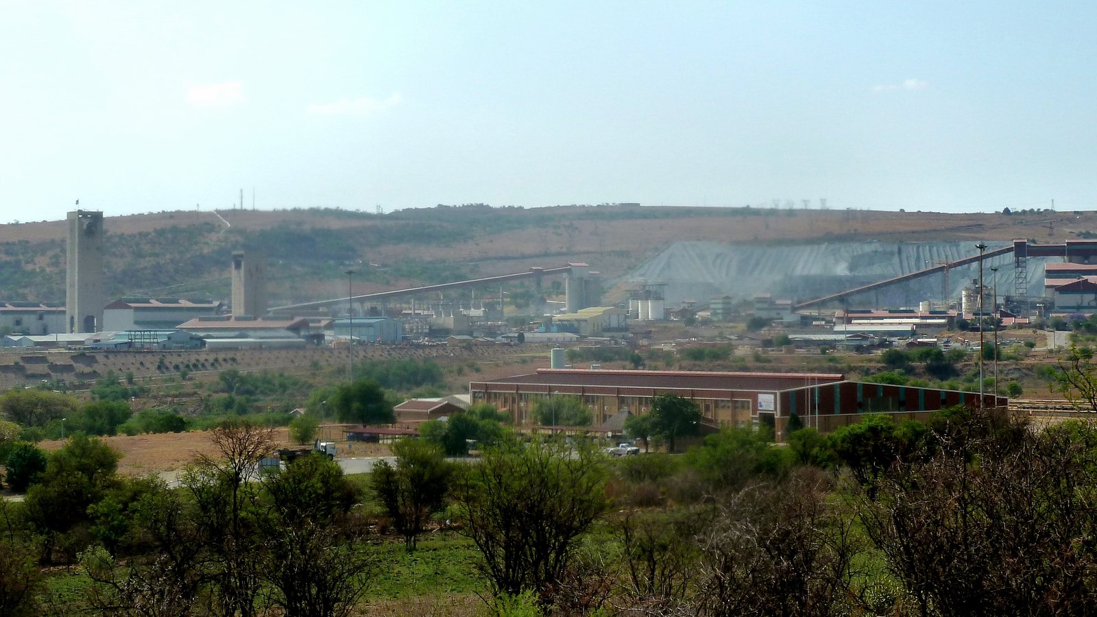 A gold mine with headframes, plant buildings and waste dumps on a ridge beyond scrubland