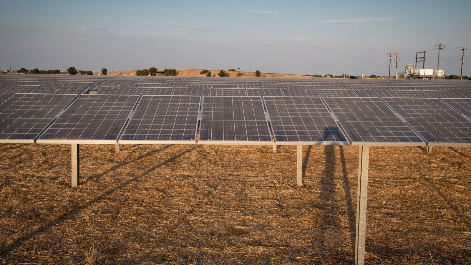 Long rows of solar panels on dry ground under a hazy sky