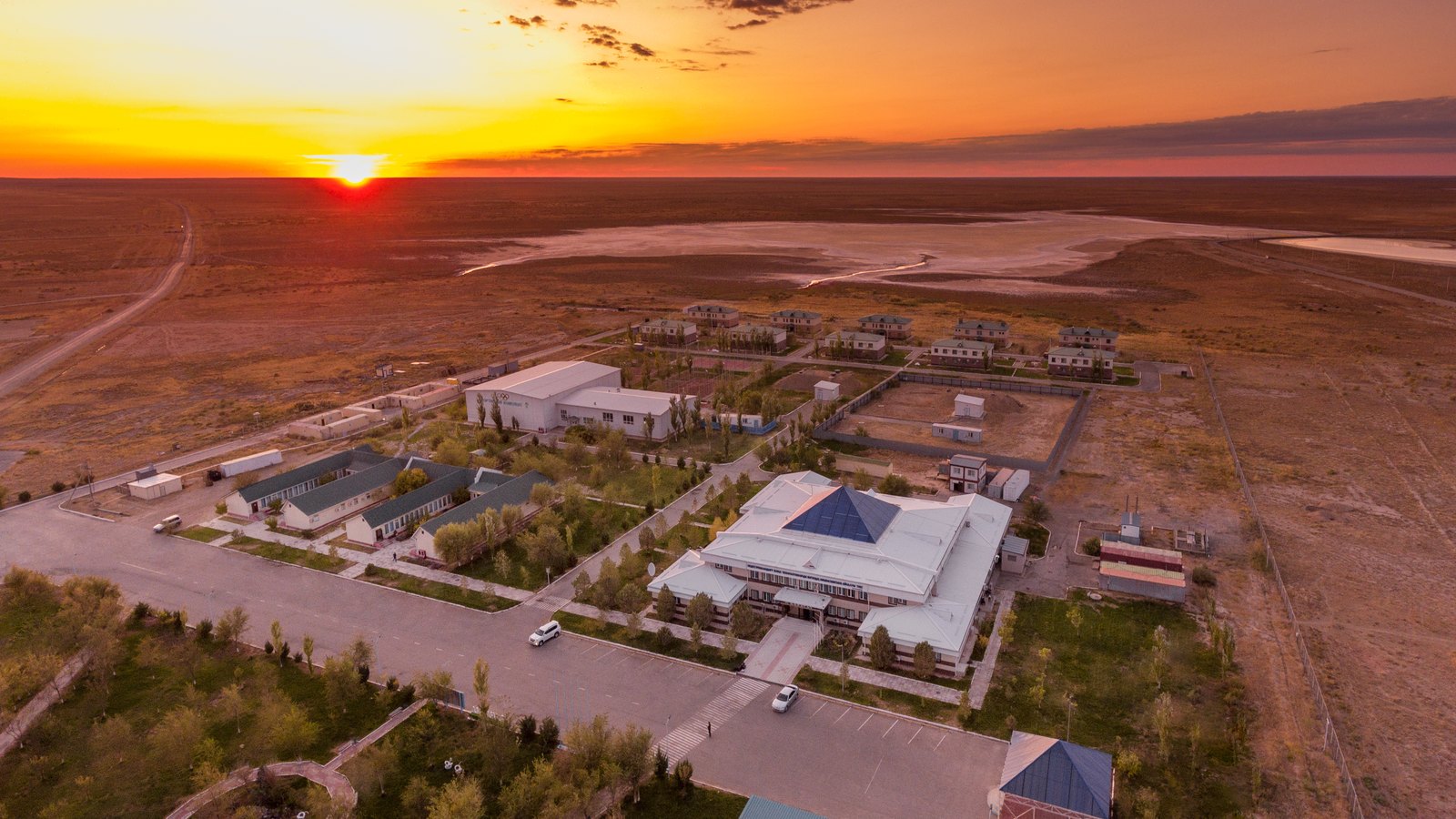 Aerial view of low-rise mine buildings and a car park on the open steppe as the sun sets on the horizon